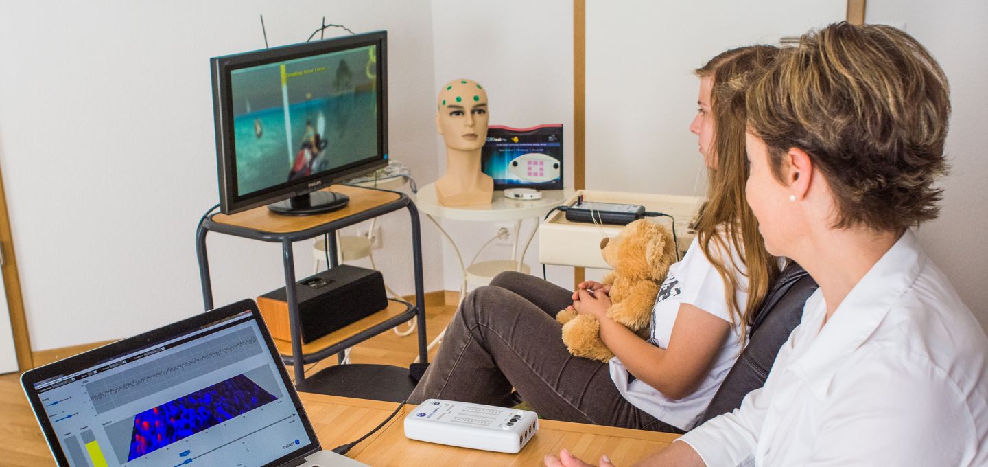 A practitioner guiding a child through an in-home neurofeedback session while brain activity displays on screens